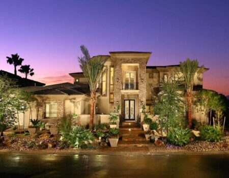 A large home with palm trees and lights in the evening.