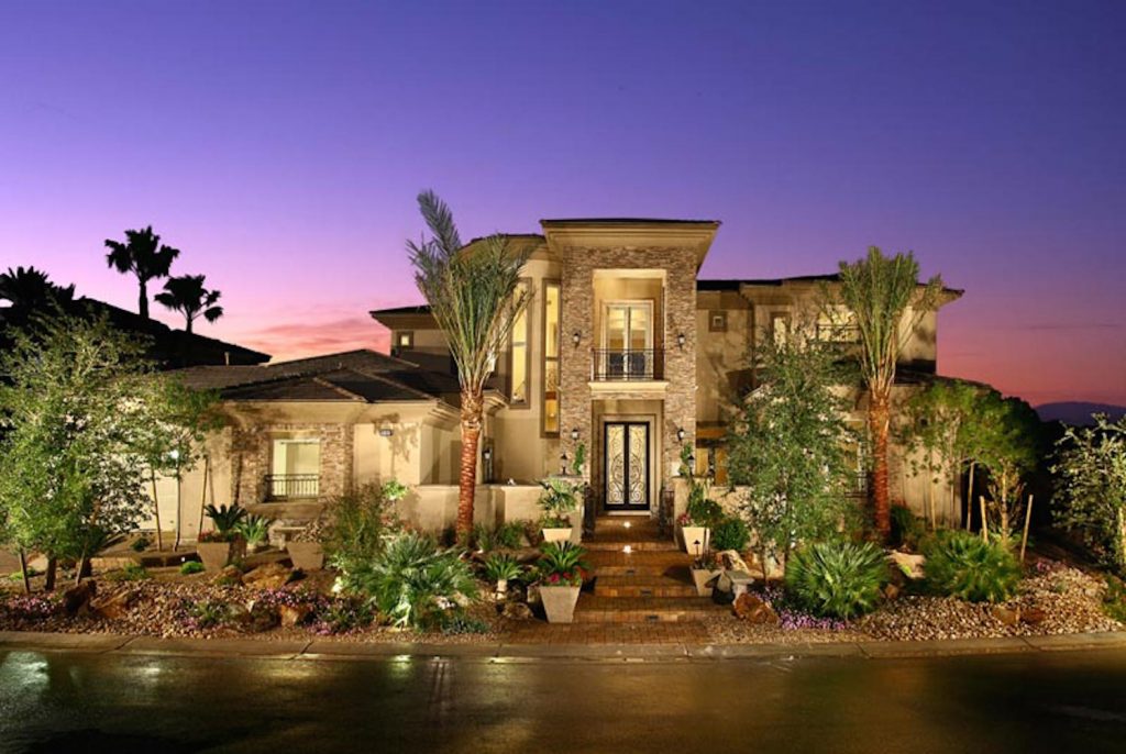 A large home with palm trees and lights in the evening. A large home with palm trees and lights in the evening.